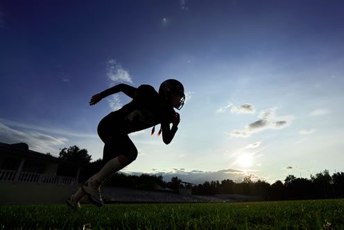 Football player running during sunset practice.
