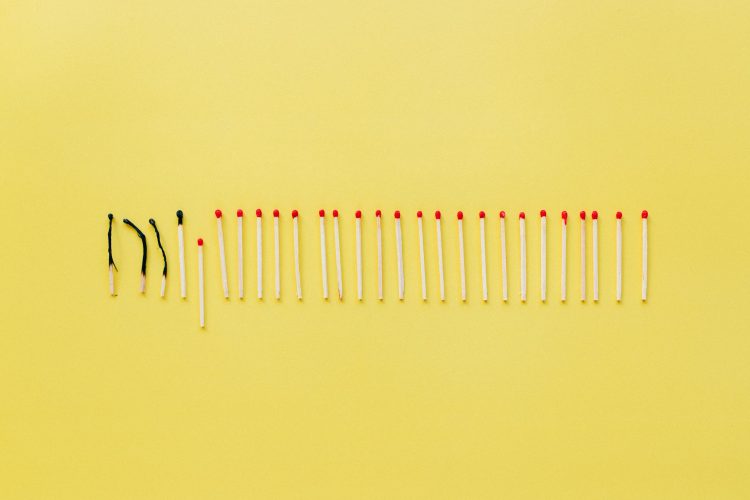 A conceptual still life photo of burnt and unlit matches on a vibrant yellow background.