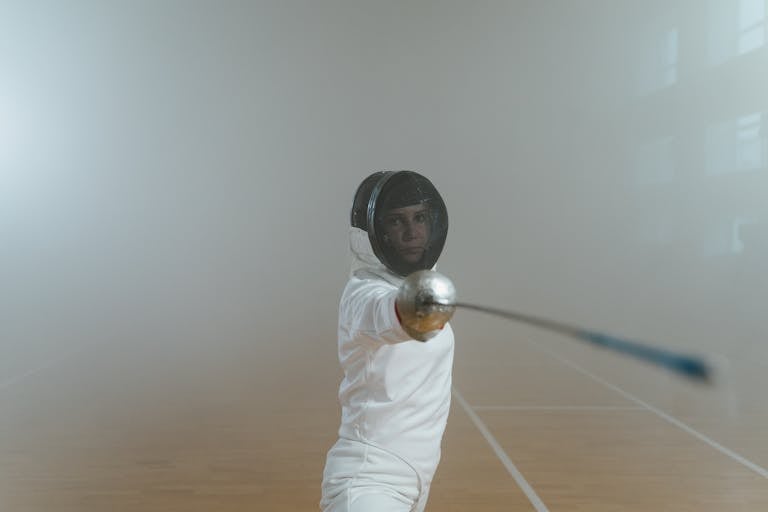 A female fencer in full gear executing a lunge in an indoor fencing salle.