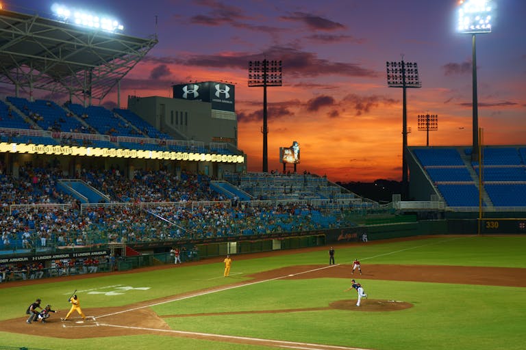 A vibrant baseball match in progress under stunning sunset skies in a crowded stadium.
