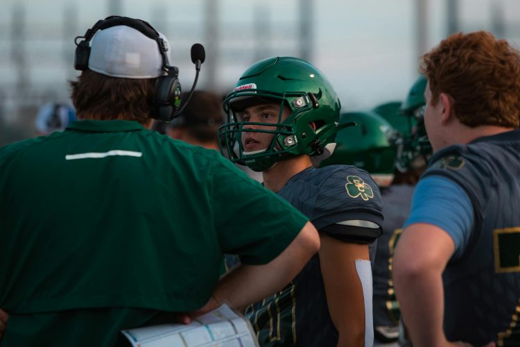 Football players and coach strategize during a game at a stadium.