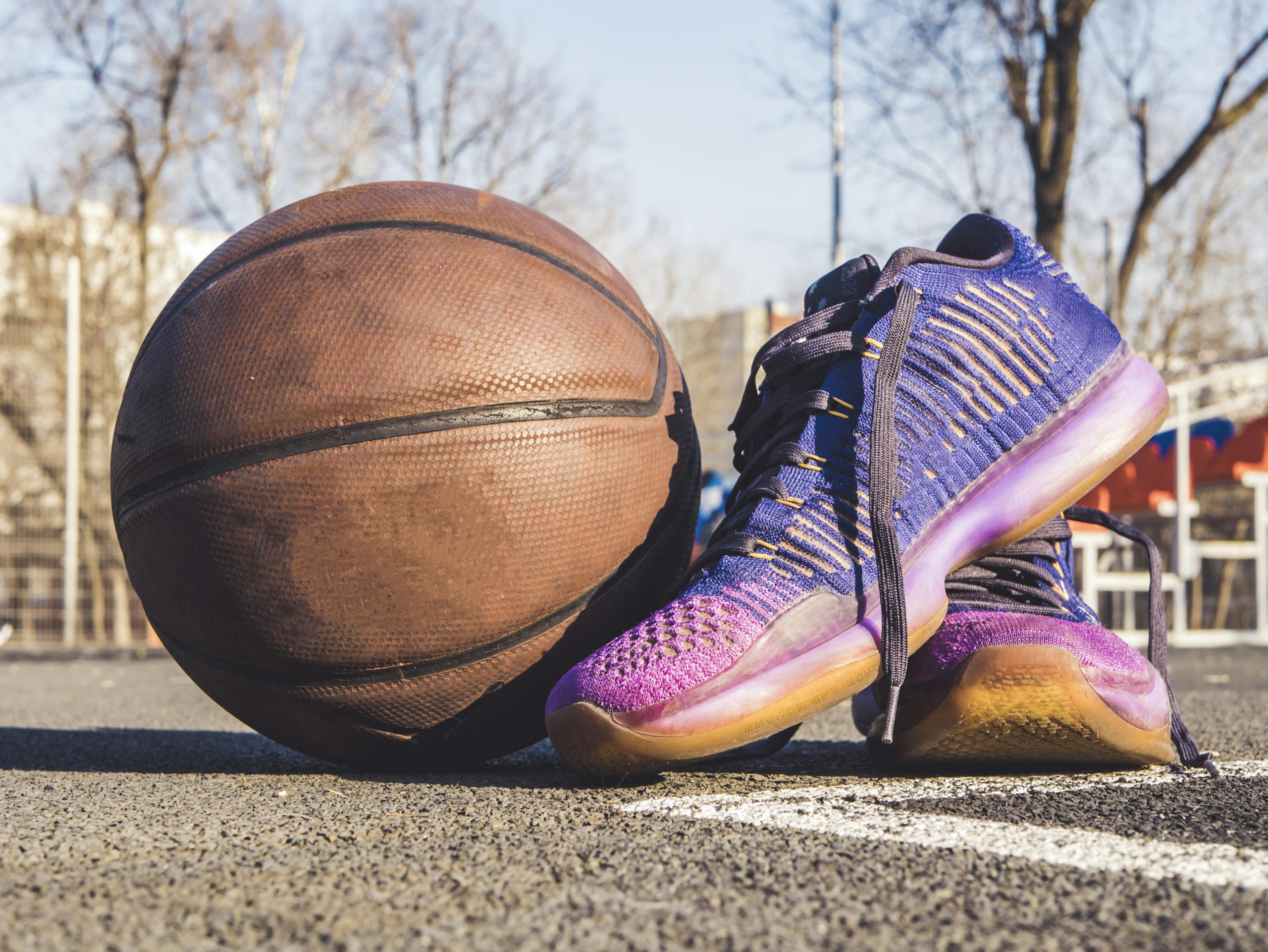 Close-up of sneakers and a basketball on an outdoor court, emphasizing sports and urban style.